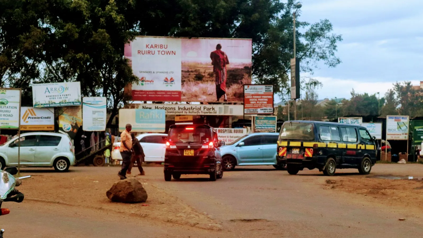 A Karibu Ruiru Town billboard above a street with cars and a matatu in Ruiru