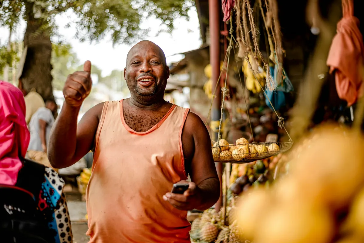 A trader at a fruit stall giving a thumbs up