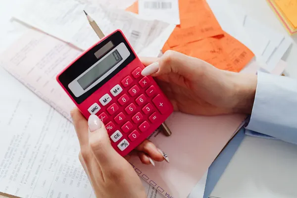 Hands working out figures on a red calculator over receipts