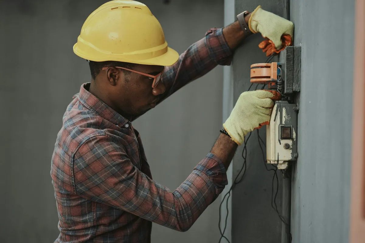 A technician in a yellow hard hat and gloves working on an electrical meter