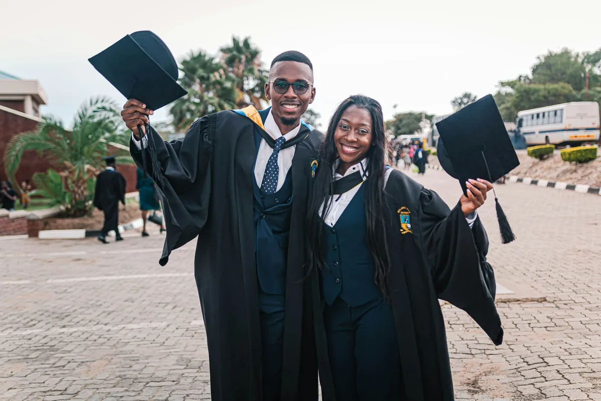 Two graduates in gowns celebrating with their caps
