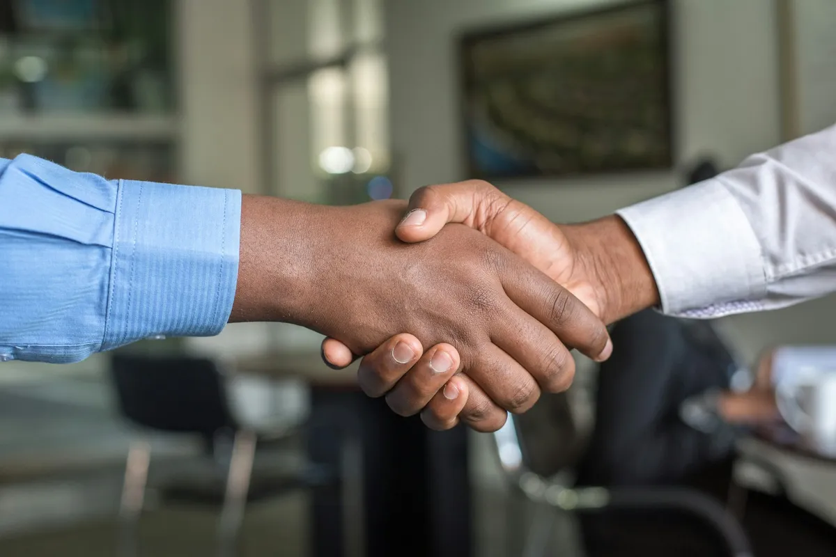 Two people in office shirts shaking hands across a table
