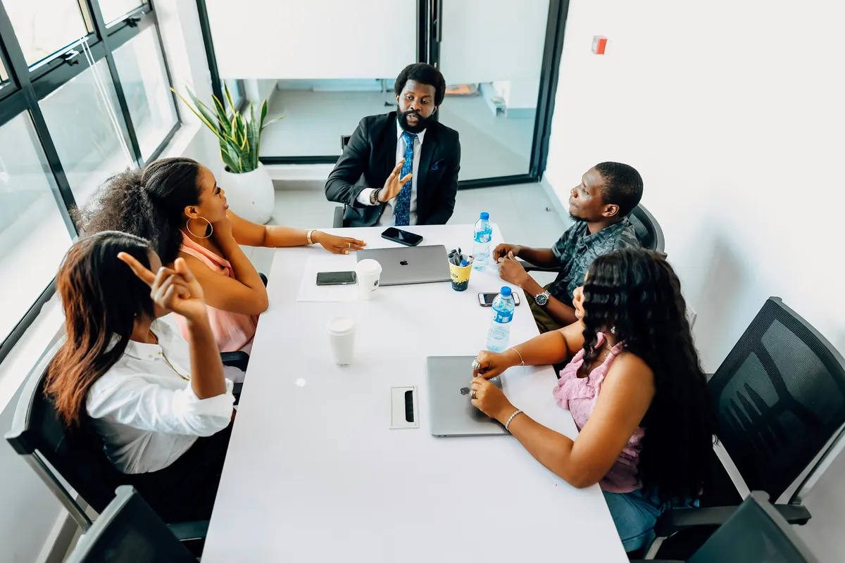 A man in a suit leads a meeting with four colleagues around an office table