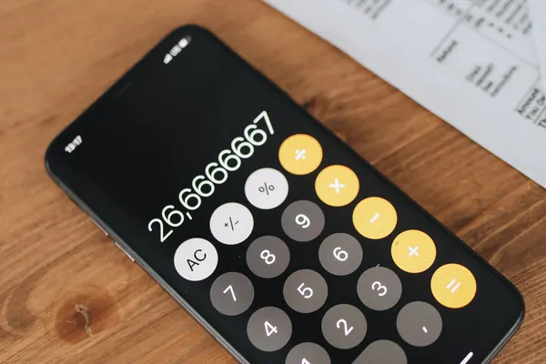 A phone calculator next to tax forms on a wooden desk