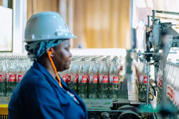 A factory worker in a hard hat watching bottles on an assembly line