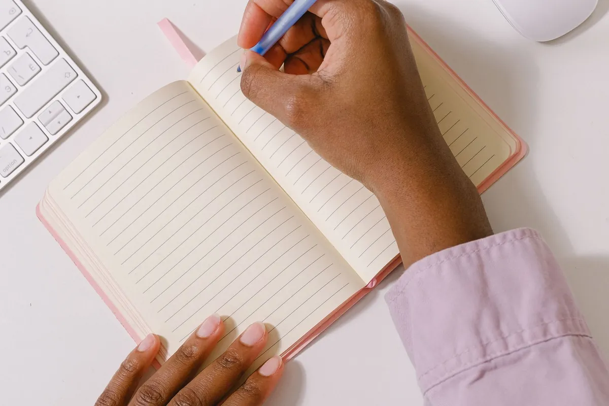A woman writing in a notebook at a desk next to a keyboard