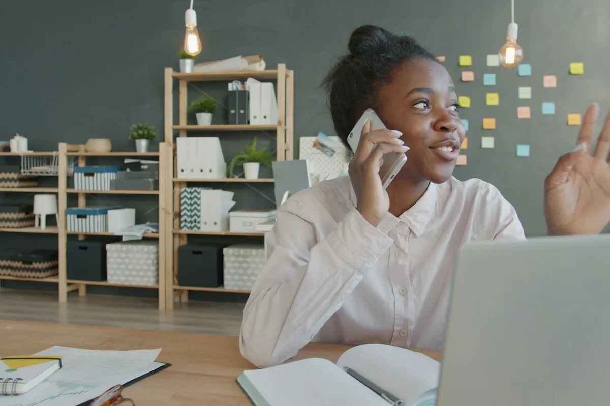 A young woman on a phone call at her desk in a bright office