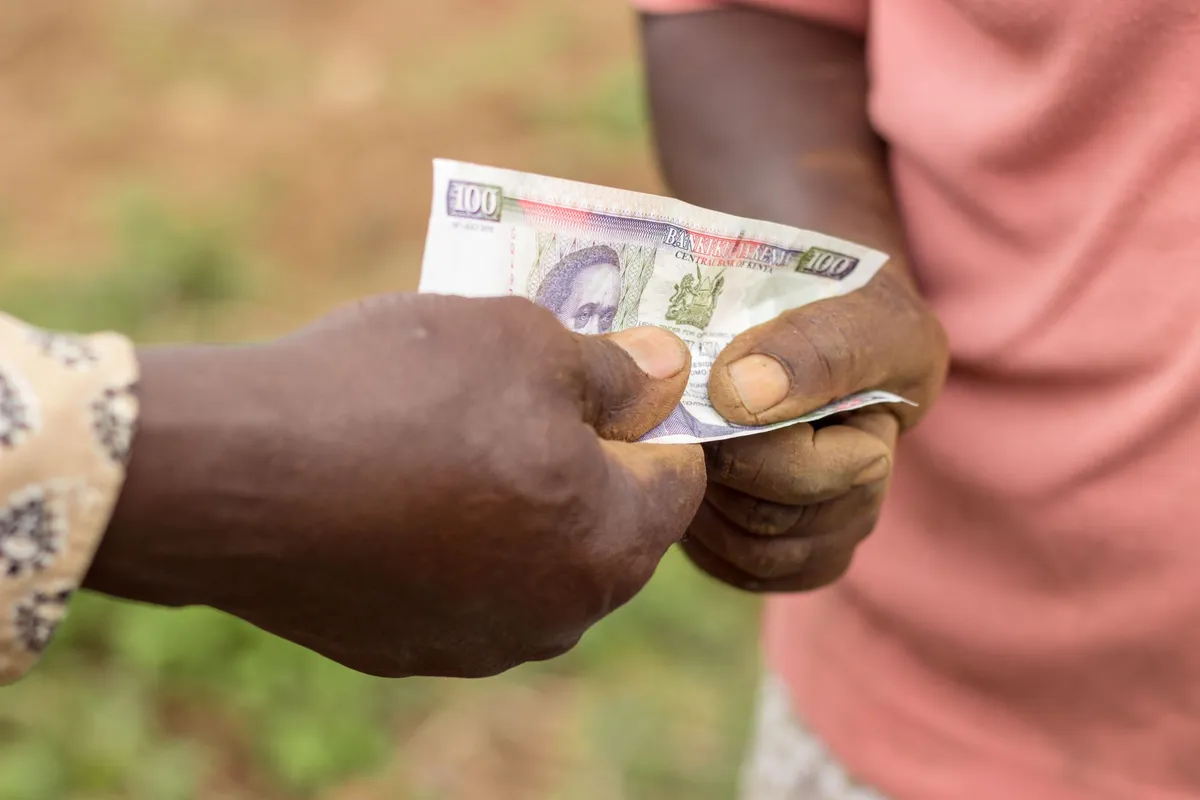 Two people exchanging banknotes outdoors in Kenya