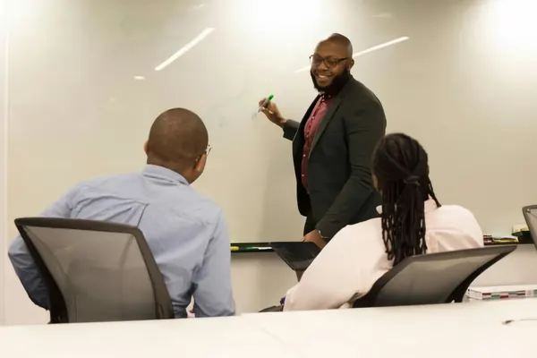 A manager presenting at a whiteboard to two colleagues