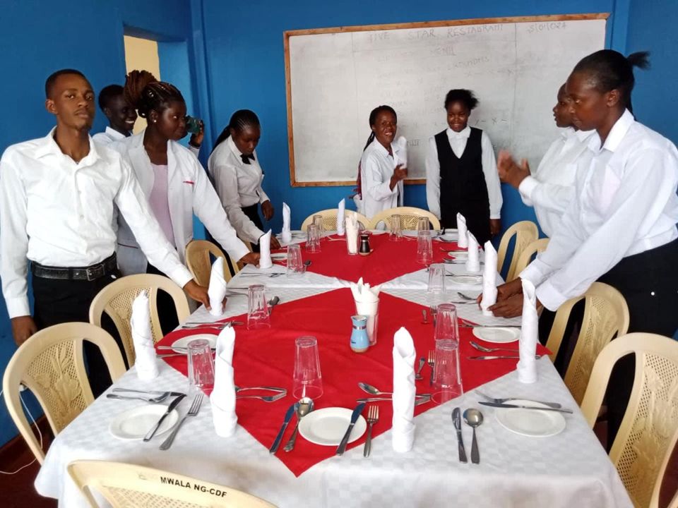 Hospitality trainees in uniform setting tables for a dining room practical